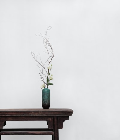 棕色木制边桌上有白色花朵和绿色陶瓷花瓶